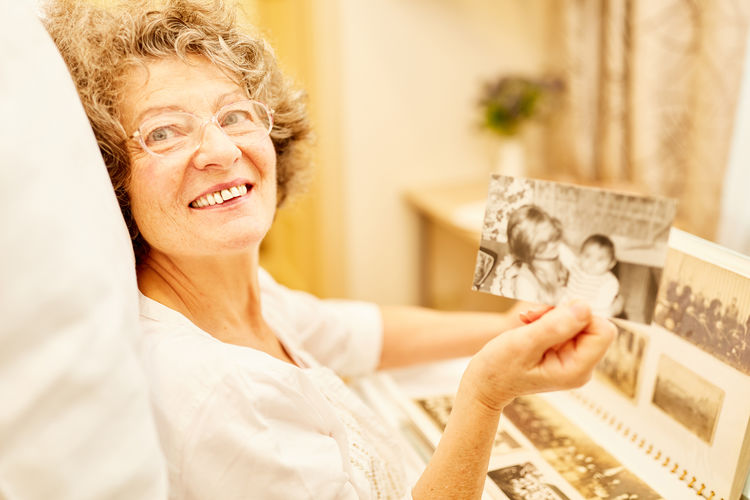Portrait of smiling woman holding old photograph while sitting at home