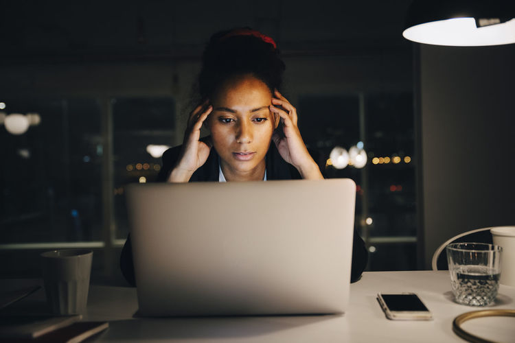 Young female entrepreneur with headache while working late in office