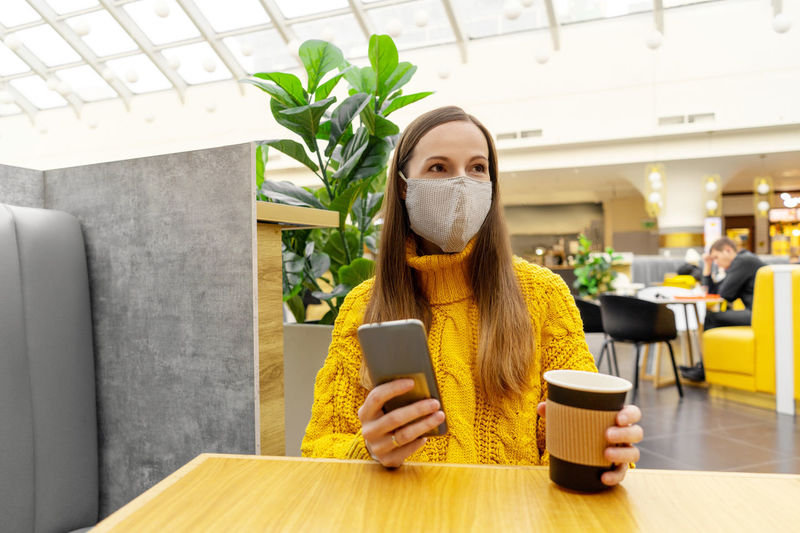 Woman wearing mask with coffee sitting in cafe