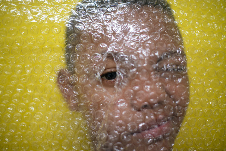 Close-up portrait of boy looking through bubble wrap