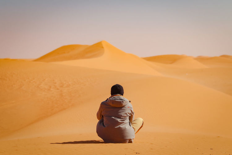 Rear view of man standing on desert against sky
