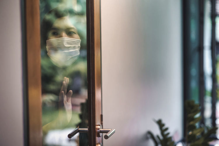 Woman wearing mask seen through glass door