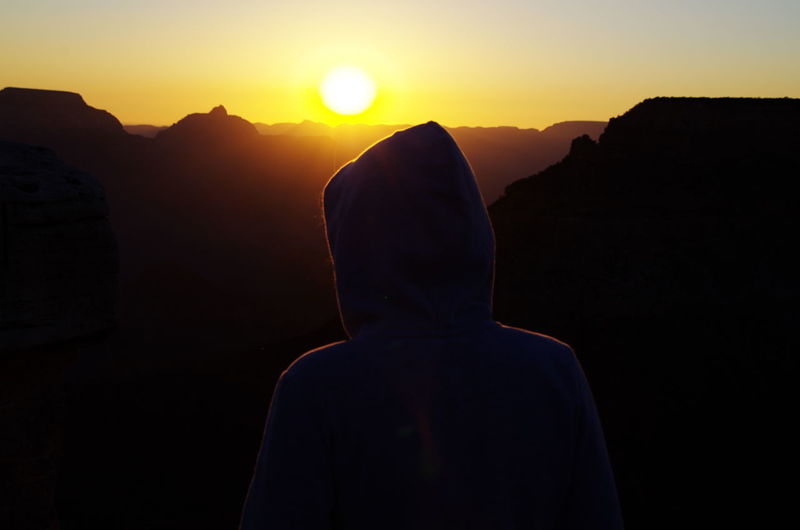 Rear view of person wearing hooded shirt against sky during sunrise