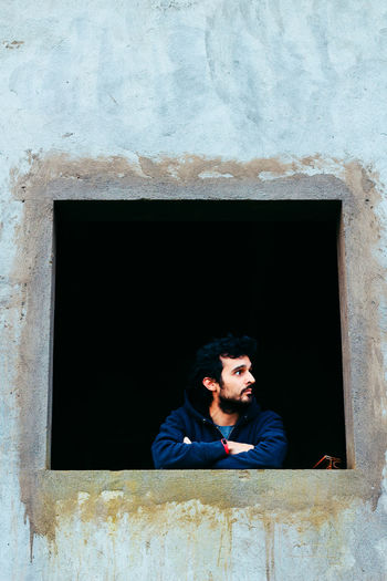 Thoughtful man looking through window by old wall