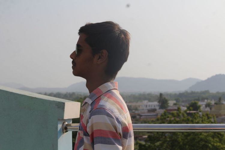 Profile shot of young man standing against railing on building terrace