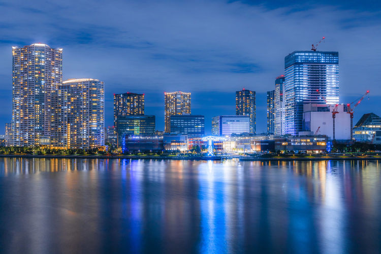 Illuminated buildings by river against sky in city at night