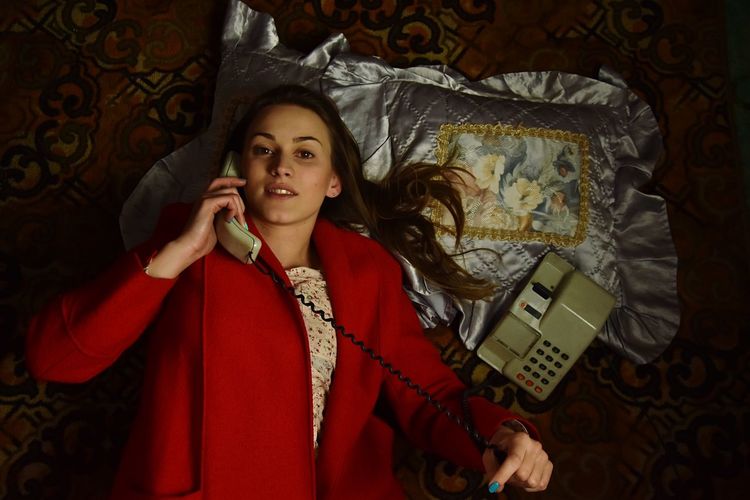 Portrait of young woman talking on telephone while lying on bed