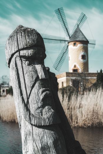 Wooden carved sculpture on a bridge with a windmill in the background