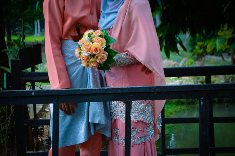 Midsection of bride and groom standing on bridge