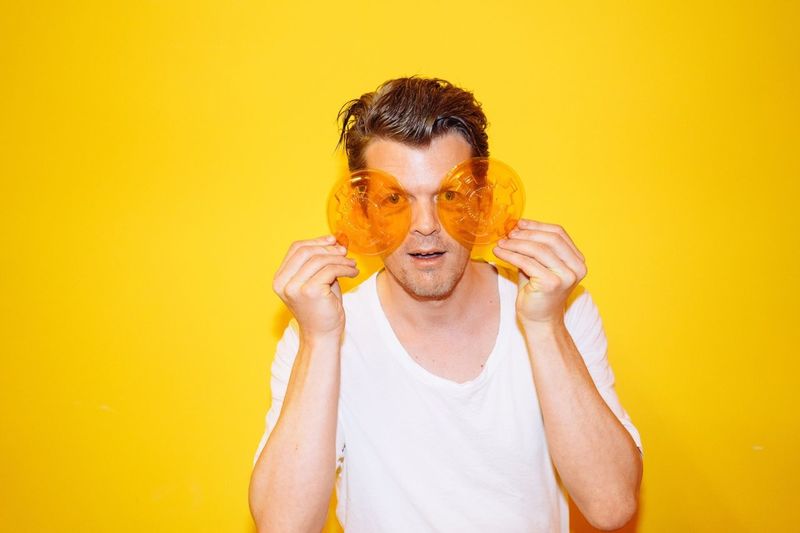Young man holding see through lids over eyes against yellow background