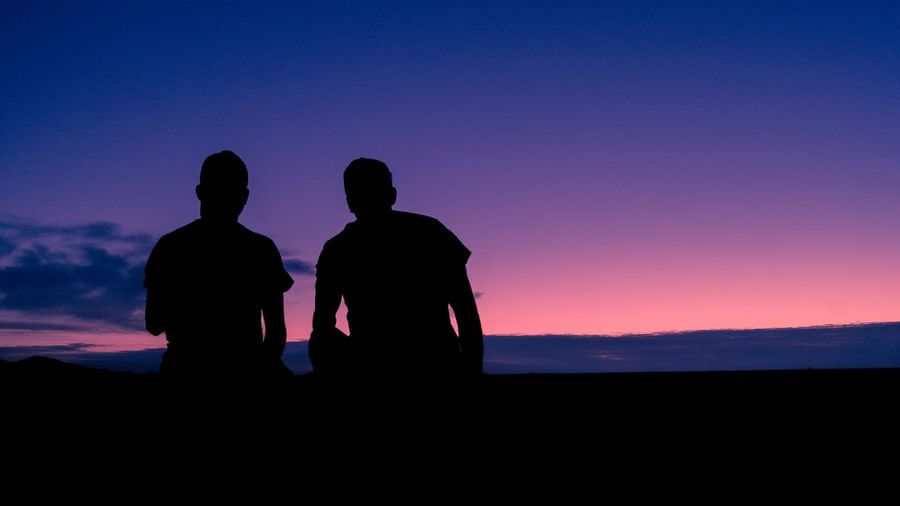 Silhouette friends against sky at dusk