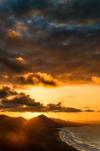 Scenic view of mountains by sea against sky during sunset