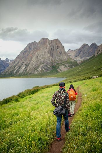 Rear view of hikers walking on grassy field by lake at tibetan plateau