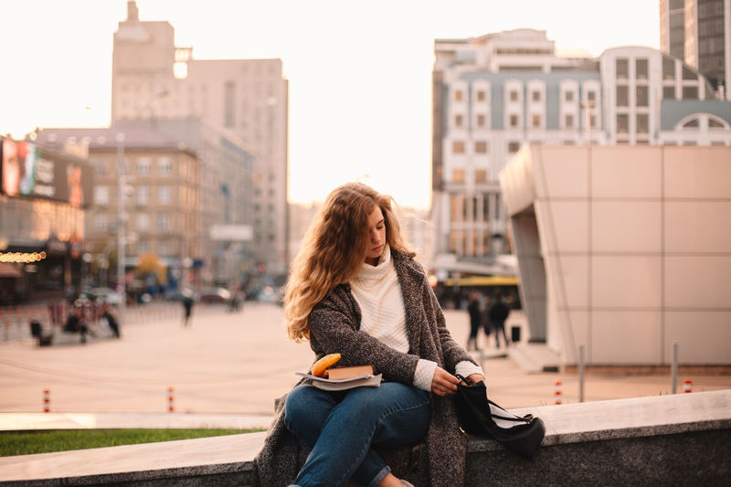 Full length of woman sitting in city against sky