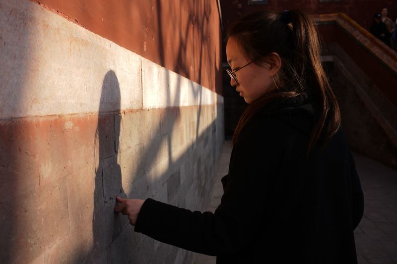 Side view of young woman standing by wall