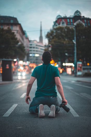 Rear view of man kneeling on road in city