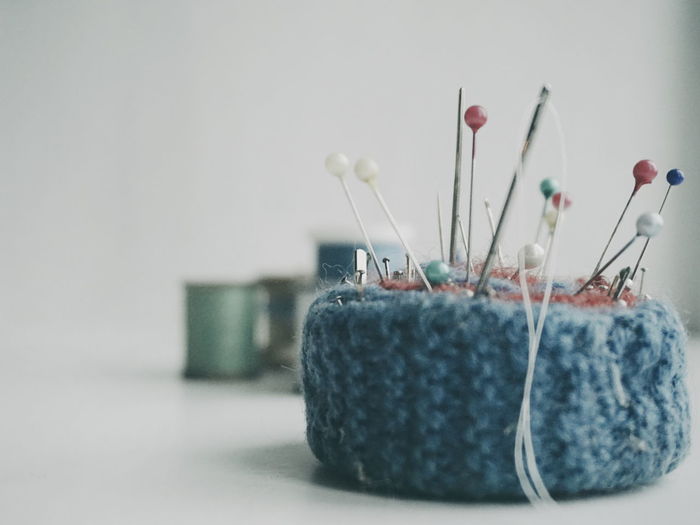 Close-up of sewing needle and thumbtacks on pin cushion over white background
