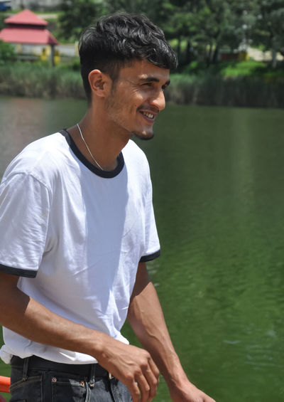 Young man smiling while standing by lake