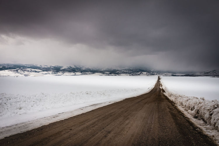 Road amidst snowcapped landscape against sky during winter