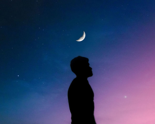 Sunset dreamy boy silhouette with the moon and stars in the colored sky