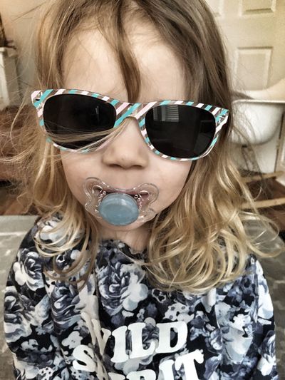 Girl with pacifier wearing sunglasses at home