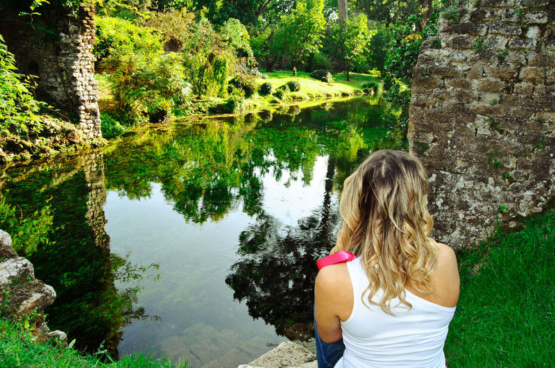 Garden of ninfa - rear view of blonde woman looking at the river
