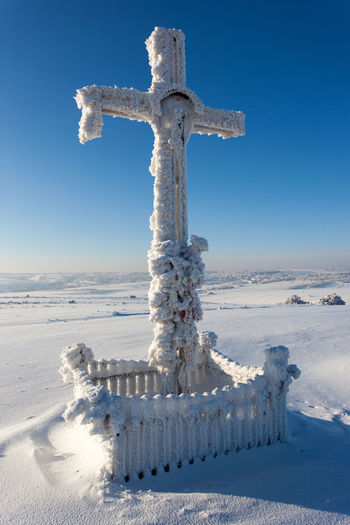 Cross on snow covered land against sky