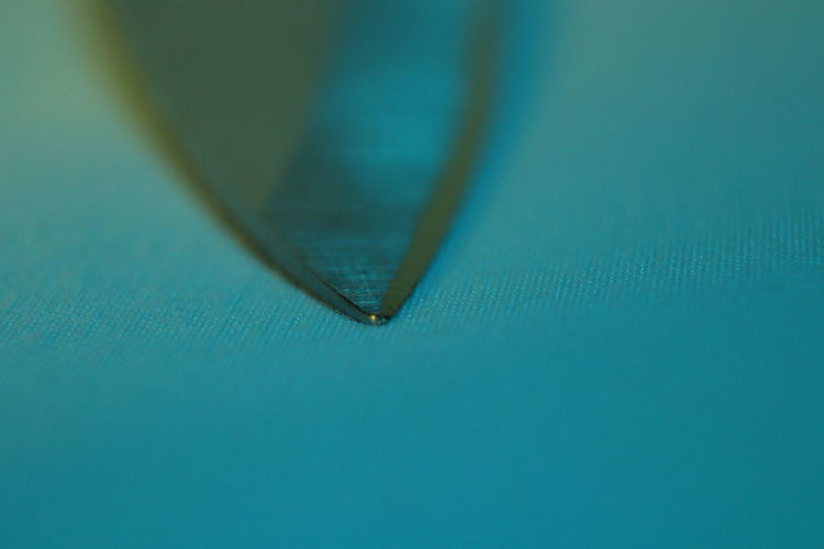 Macro close up of a point of a knife lit with subtle blue light. the knife is lain on it side.