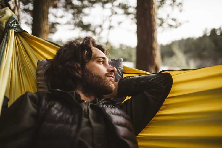 Contemplating man looking away while lying over hammock in forest