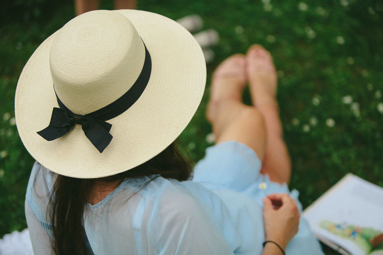 Rear view of woman wearing hat sitting on grassy field in park