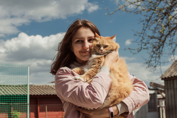 Portrait of young woman with cat against sky