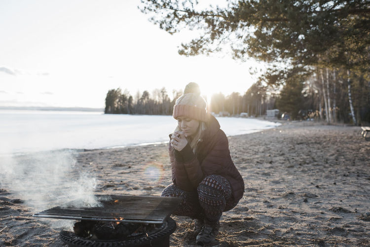 Woman warming up by a fire at the beach in winter in sweden