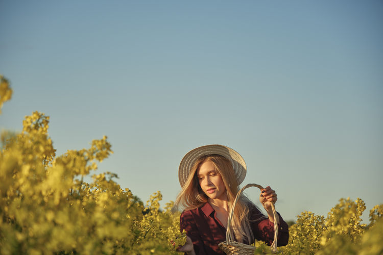 Happy young attractive woman in hat and purple dress on rapeseed field