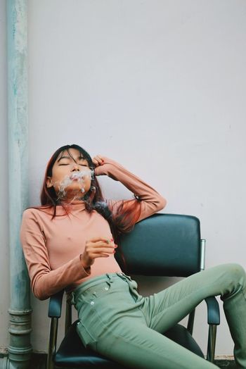 Woman sitting on chair against wall
