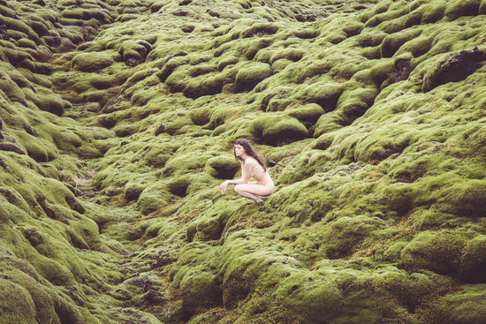 Side view of naked woman crouching on mossy rock