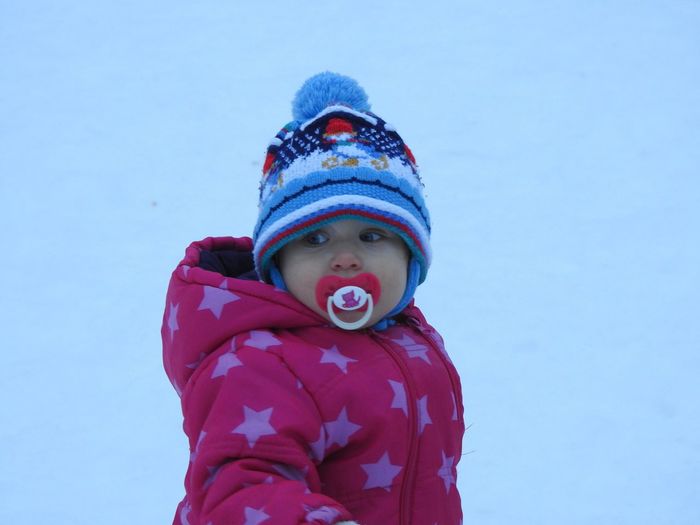 Close-up of girl in warm clothing sucking pacifier against clear sky