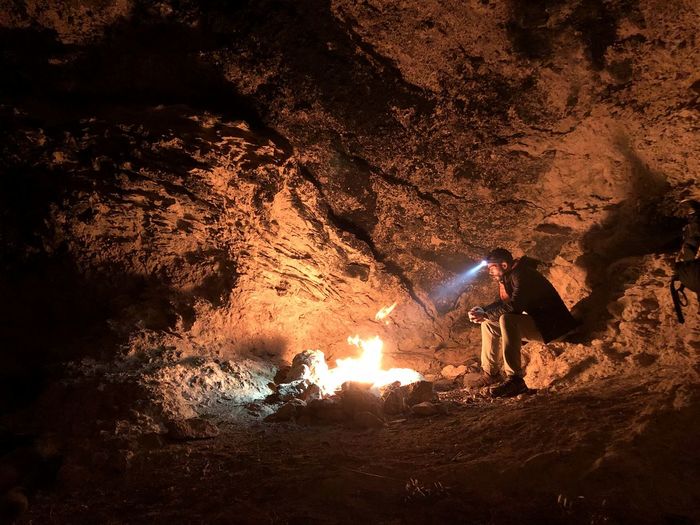 Full length of man sitting by fire in cave