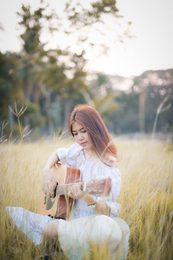 Woman playing guitar while sitting on plant