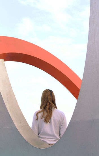 REAR VIEW OF WOMAN STANDING ON ARCH AGAINST SKY