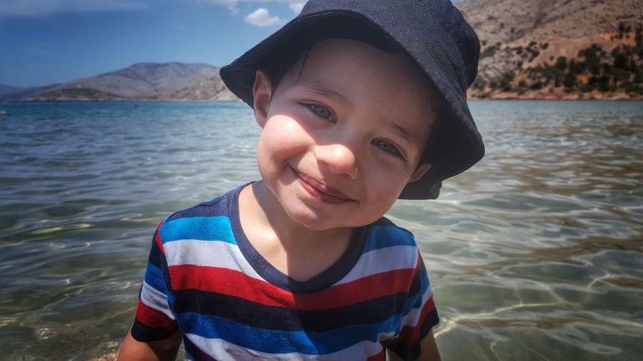 Portrait of smiling boy standing against river on sunny day