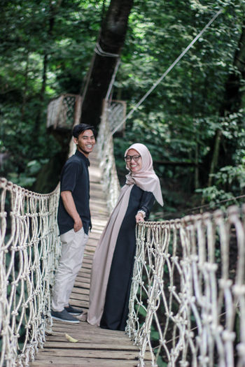 Man and woman on footbridge against trees in forest