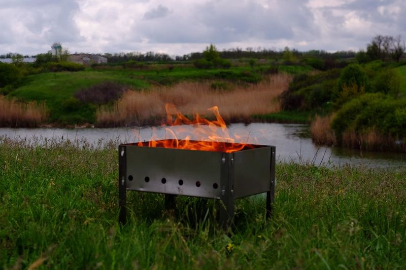 Fire burning in pit on grass against sky