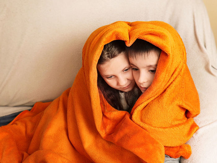 Children brother and sister froze and covered their heads with an orange blanket. child friendship 