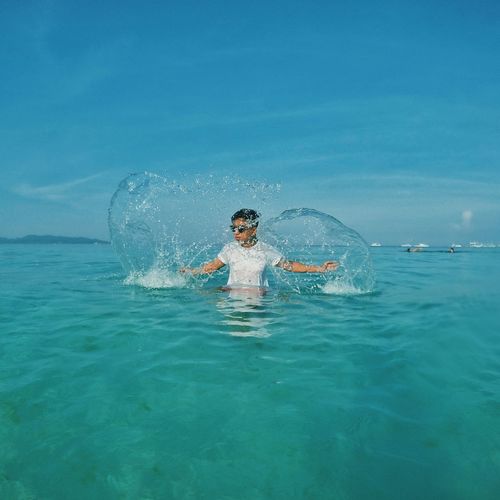 Playful teenage boy in sea against blue sky
