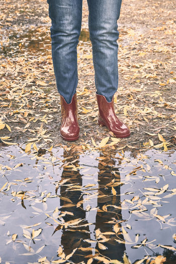 Red rubber boots in front of a puddle with yellow leaf in autumn. rain concept