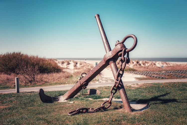 Rusty historic anchor with chain on field against clear sky
