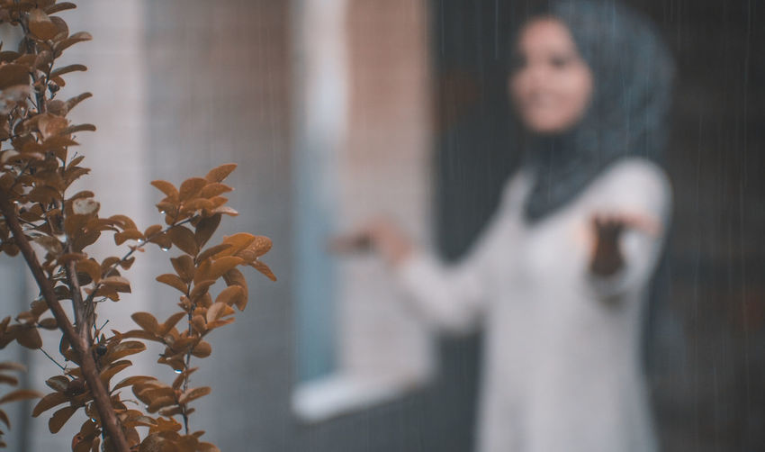 Woman enjoying rainfall with plant in foreground