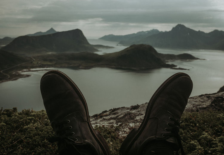 Low section of shoes by lake against mountain range