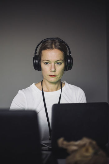 Female it professional with headphones typing on laptop in creative office