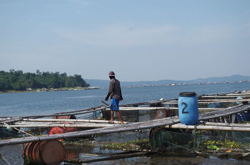 Side view of man walking on bamboos over lake